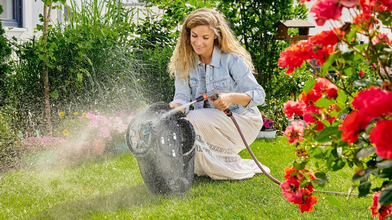 A woman hosing down the underside of a robotic lawnmower