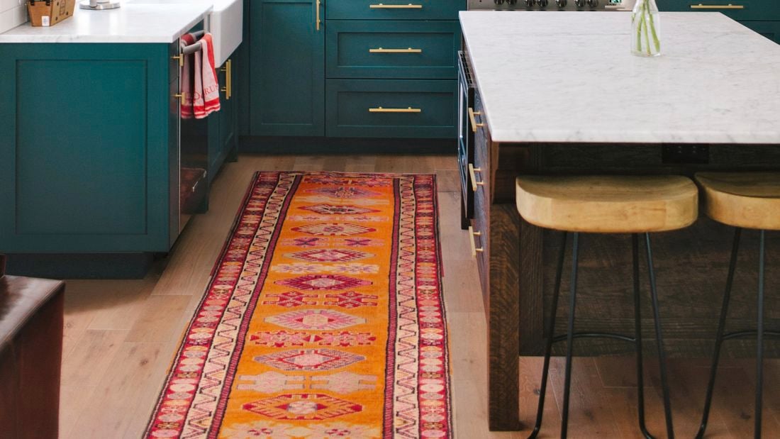 A country themed kitchen with teal painted cabinets, brass fittings and a long woven rug