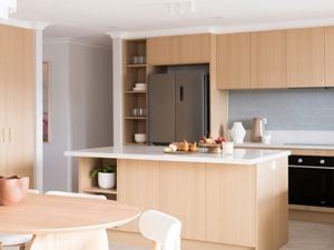 A modern kitchen features light wood cabinetry, a large island with a white benchtop, creating a clean and stylish space.