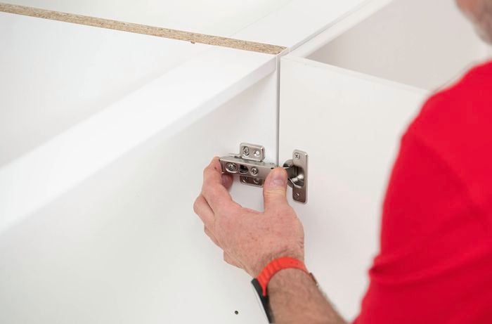 A person is attaching a cabinet door to the frame by connecting the hinge into the mounting plate.