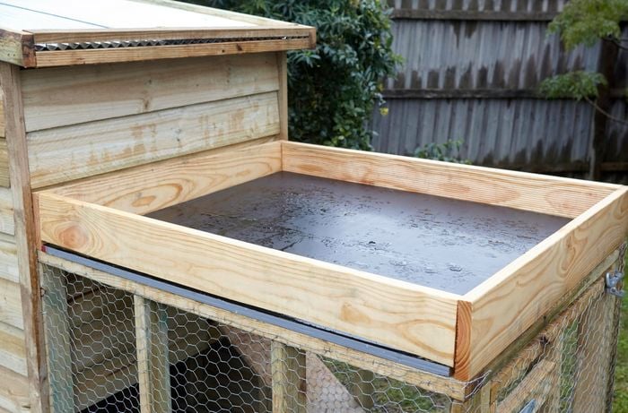 An empty planter box positioned on the roof of a chicken coop, lined across the bottom with black plastic