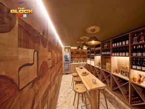 A bar area with lot of bottles of wine in it with a table and stools around it.