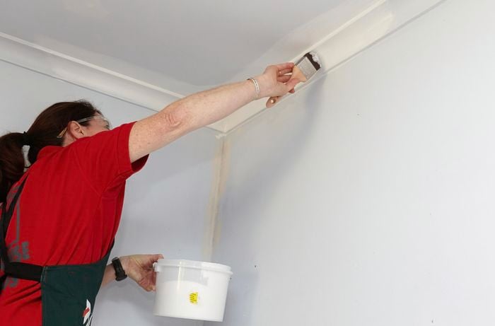 A person on a ladder painting cornice with a paintbrush