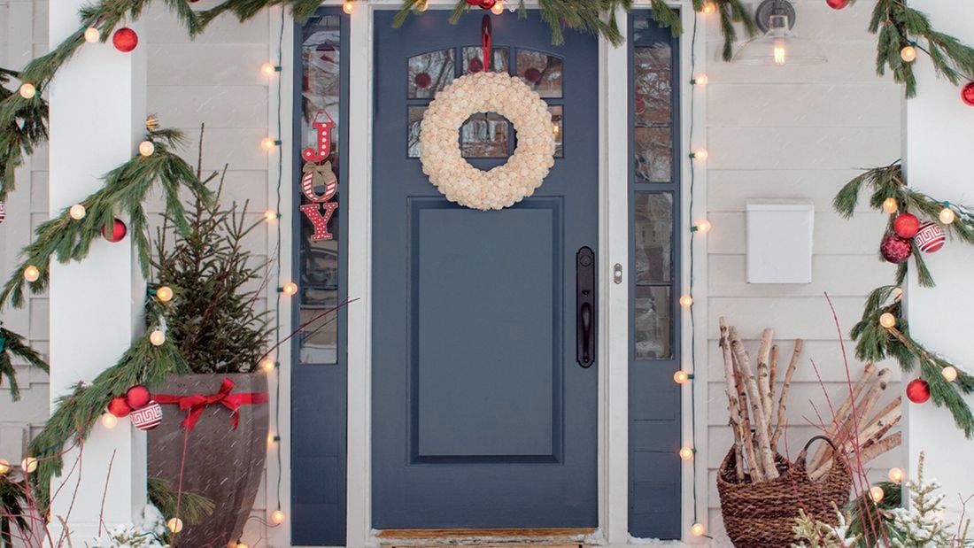 A festive front door decorated with a wreath, garland, ornaments, and Christmas lights.