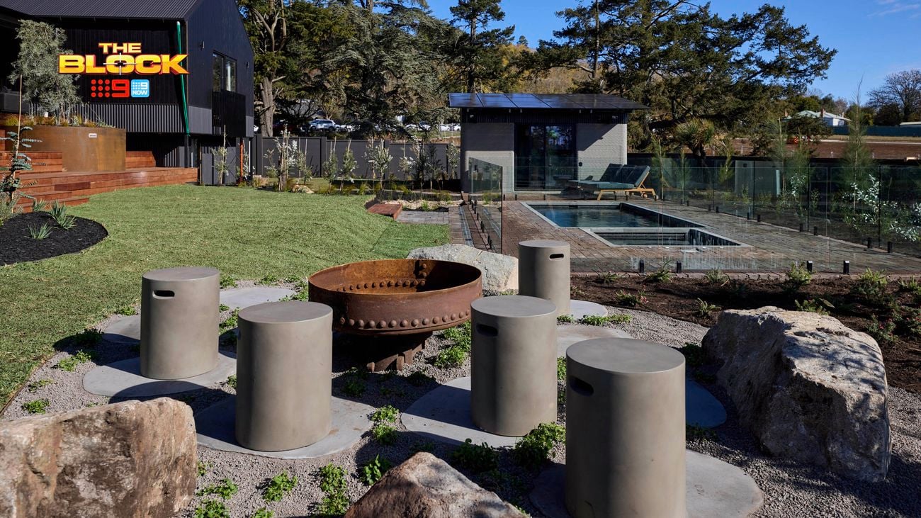 The back of a house with a firepit, a rocked area, a pool and an outdoor room in it.