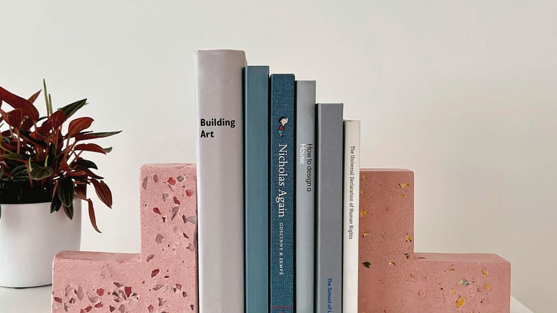 Pink terrazzo bookends with books in the middle and a potted plant.