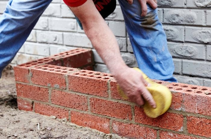 Person wiping excess mortar from a brick planter box