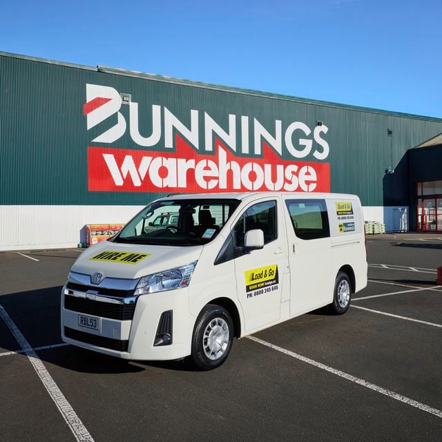 White rental van with “Load & Go” signage parked in front of a Bunnings Warehouse store exterior on a clear day.