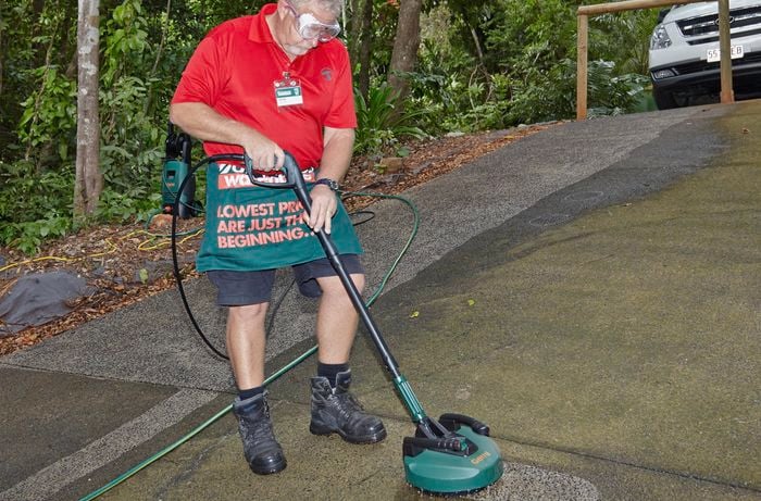 A person cleaning a driveway using a patio cleaning nozzle on a high-pressure washer