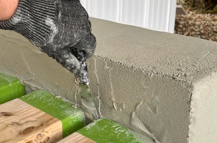 A person using a scraper to smooth out render