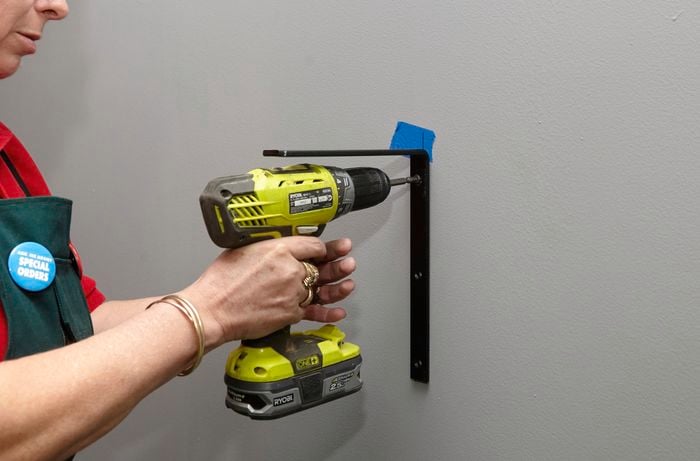 A person attaching a wall bracket to a wall using a cordless driver