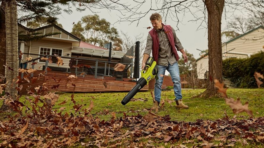 An individual blowing leaves in a garden using a cordless blower.