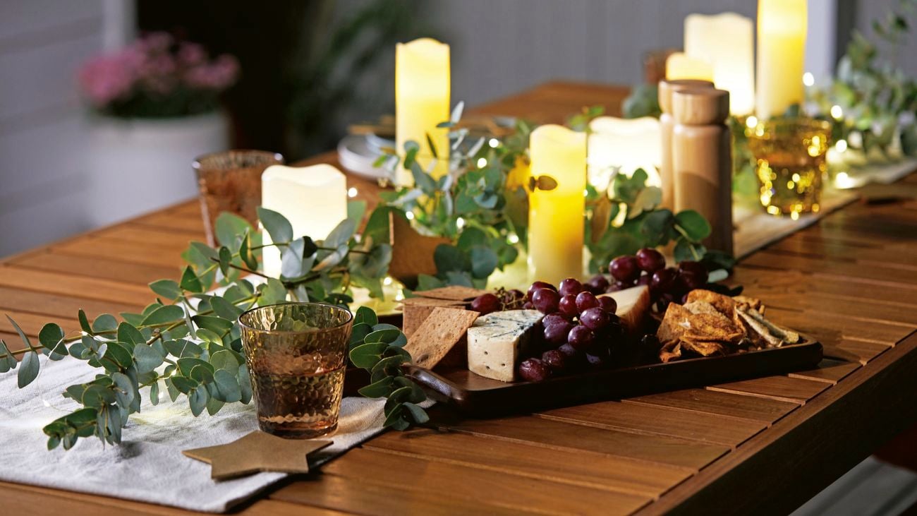 A festive, outdoor table setting at night time, set with candles and foliage.