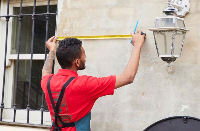 Person holding a pencil and using a retractable ruler to measure a wall