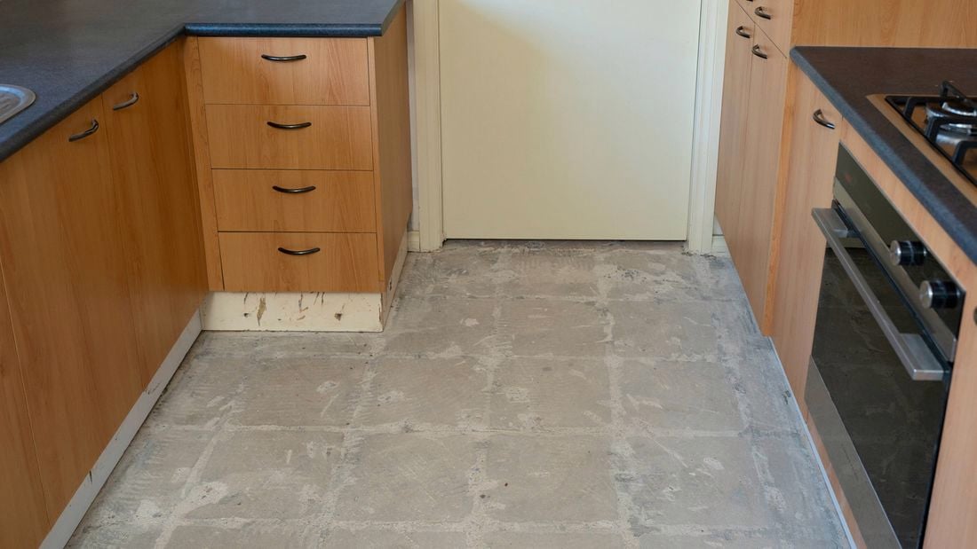 A kitchen floor exposes a clean concrete surface after the tile removal surrounded by wooden cabinets.