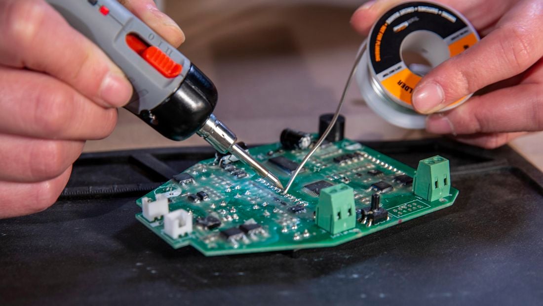 A soldering iron melts metal alloy onto a circuit board. 