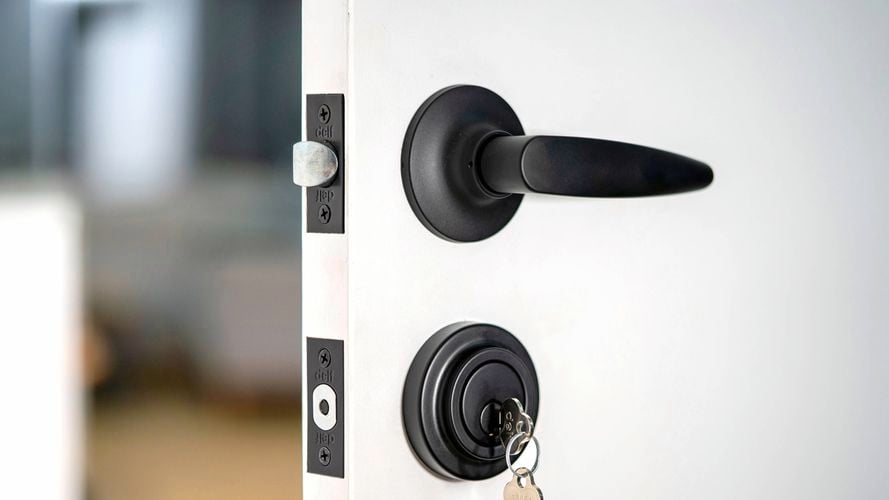 A matt black door handle and with a key to the lock on a white door from Delf