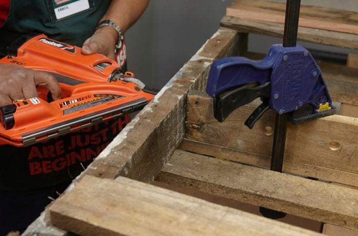 A person fixing a shelf into a timber frame using a nail gun
