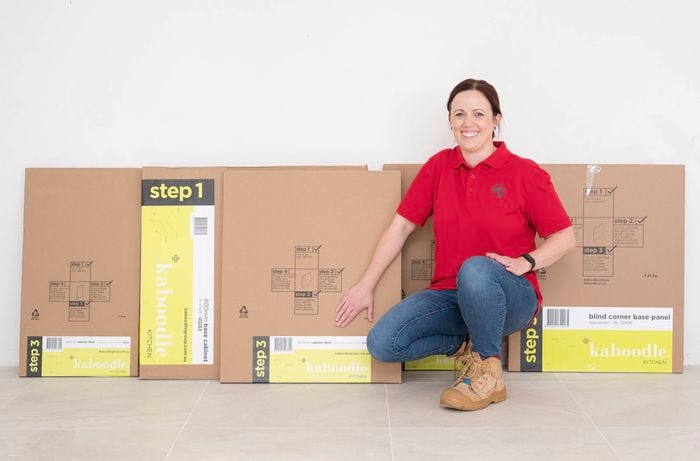 A Bunnings Team Member is kneeling beside flat-pack cabinet boxes ready for assembly.