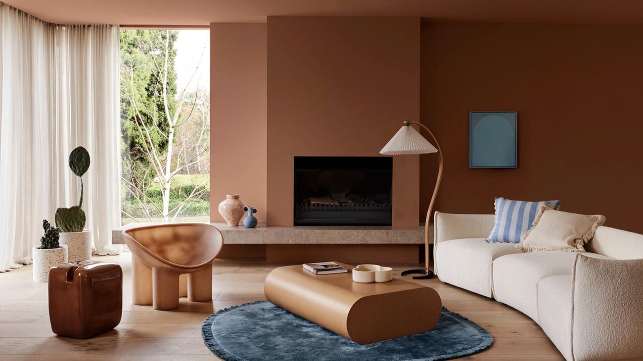Lounge room with brown walls, a cream couch, lamp on a stand, a coffee table on a rug and a painting on a wall.