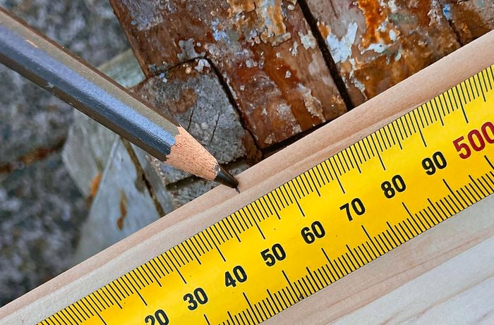 A wooden panel with a ruler measuring the side. A pencil is marking a line in the middle.