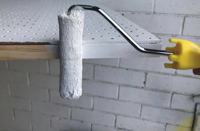 A pegboard being painted white with a paint roller