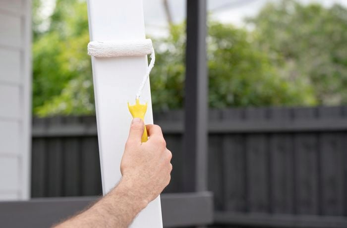 A shade sail post being painted white with a paint roller
