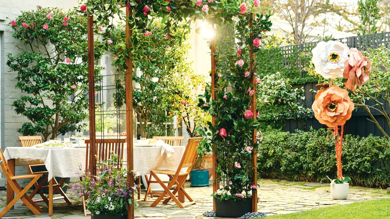 A garden arch draped with flowering vines beside an outdoor dining table.