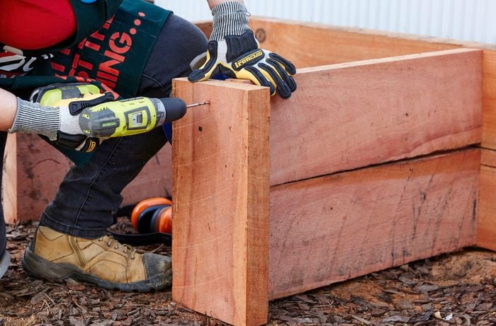 Guides being secured to the front of a sleeper compost bin with a power drill