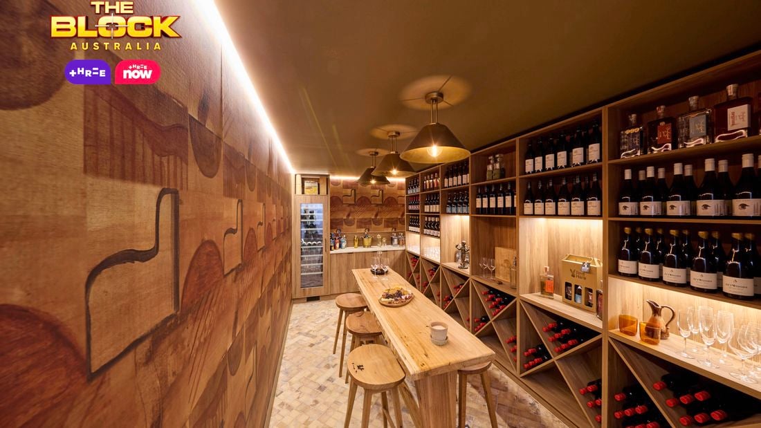 A bar area with lot of bottles of wine in it with a table and stools around it.