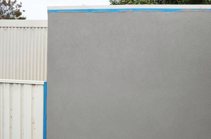 A wall covered in render, with the painter's tape yet to be removed