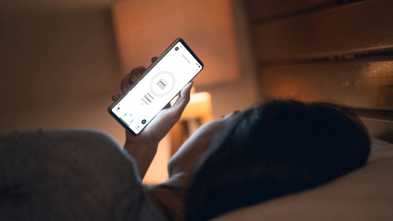 Woman laying in bed checking her Chamberlain myQ app on a phone