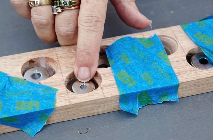 A person pressing magnets into holes in a piece of timber filled with silicon