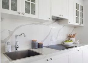 Modern white bathroom with white cabinetry, marble look splashback and benchtop, electric stovetop and stainless steel tapware.