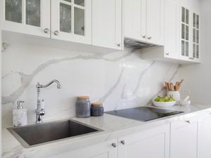Modern white bathroom with white cabinetry, marble look splashback and benchtop, electric stovetop and stainless steel tapware.