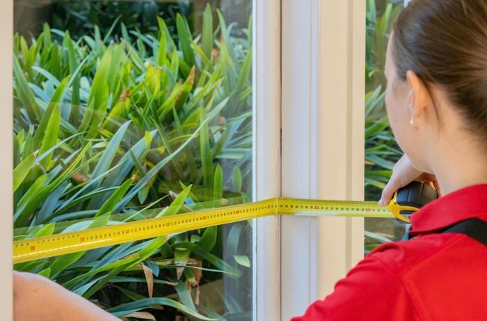 A Bunnings Team Member holding a tape measure against a window