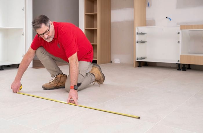 A Bunnings Team Member is using a measuring tape to mark the measurements on the tiled floor for cabinet installation.