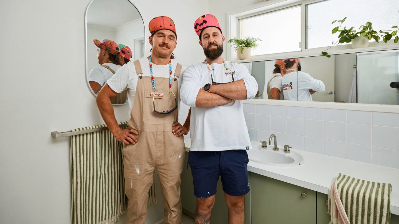    a {     text-decoration: none;     color: #464feb; } tr th, tr td {     border: 1px solid #e6e6e6; } tr th {     background-color: #f5f5f5; }     Two men standing side by side in a bathroom in front of a vanity with a sink and mirror, both wearing colourful patterned caps and casual workwear, with striped towels, a round wall mirror, and indoor plants visible around the bright, tiled space.