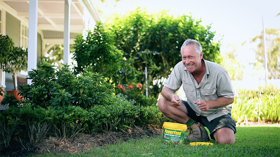 Man kneeling in garden with tub of plant food