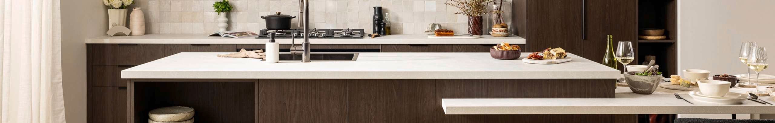Brown modern kitchen with a white marble benchtop and beige splashback behind the stove top.