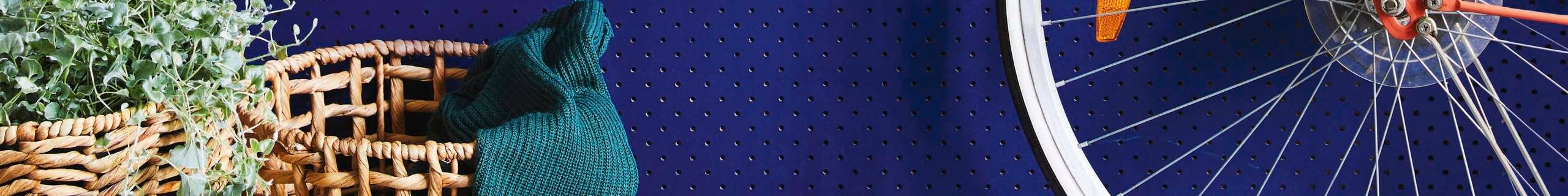 A blue pegboard wall with a shelf, bike, hat, keys and bag hanging up on it.