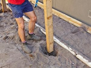 Person lowering a fence post into a hole beside a string line