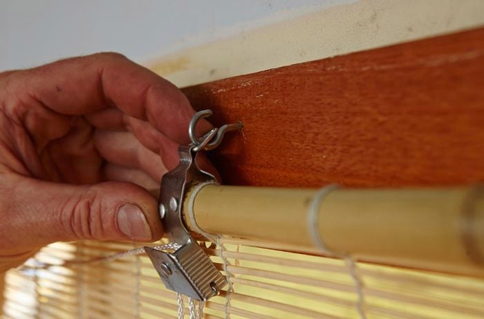 Person attaching screw in hook for blinds to a window frame.