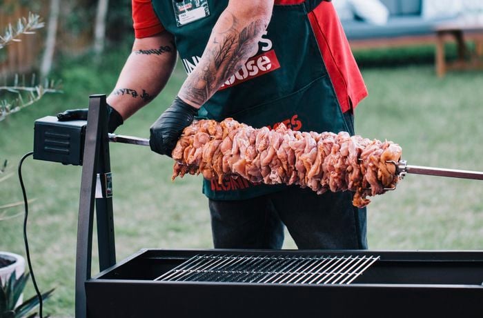 Person attaching a rotisserie rod full of meat to a spit roaster