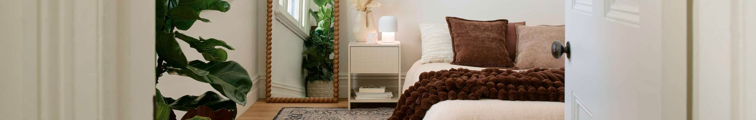 Bright bedroom with low bed, neutral bedding, patterned rug, mirror, and indoor plants.