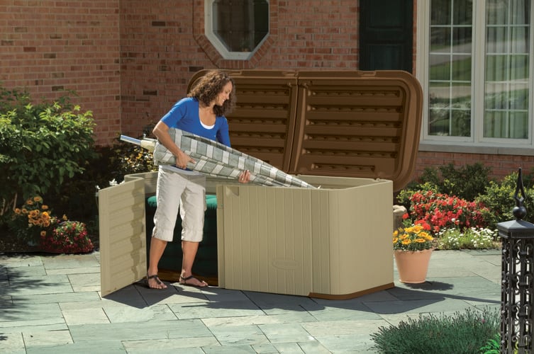 Woman in an outdoor paved area placing a beach umbrella into storage cabinet with lid and doors