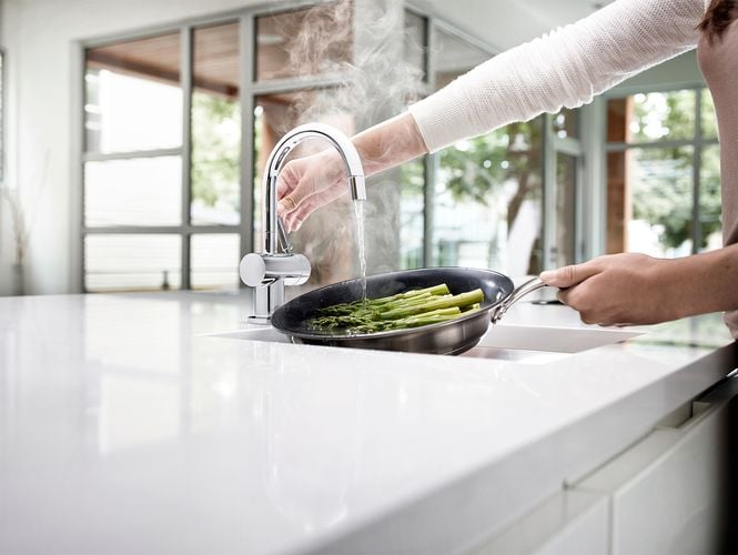 Person adding water from tap to pan of asparagus