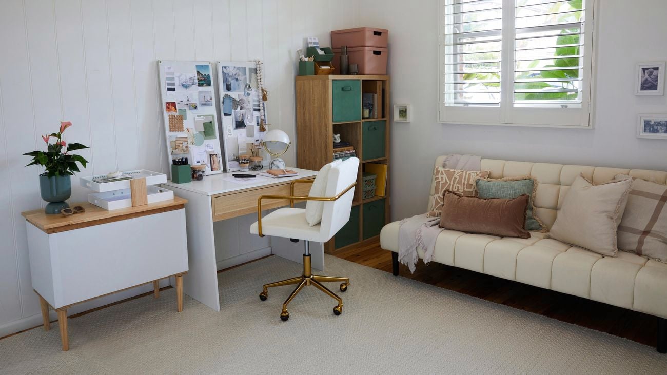 Home office nook with white feature wall, timber desk, timber filing cabinet/cubes, computer screen, white chair and white lounge.