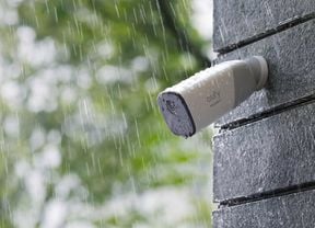 Close up of security camera on brick wall outside in rain.