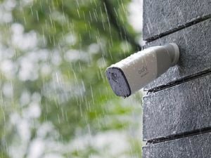 Close up of security camera on brick wall outside in rain.